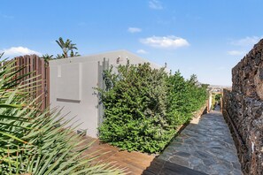Un estrecho sendero de piedra que conduce a un edificio con fachada blanca y una cerca de madera a un lado.
