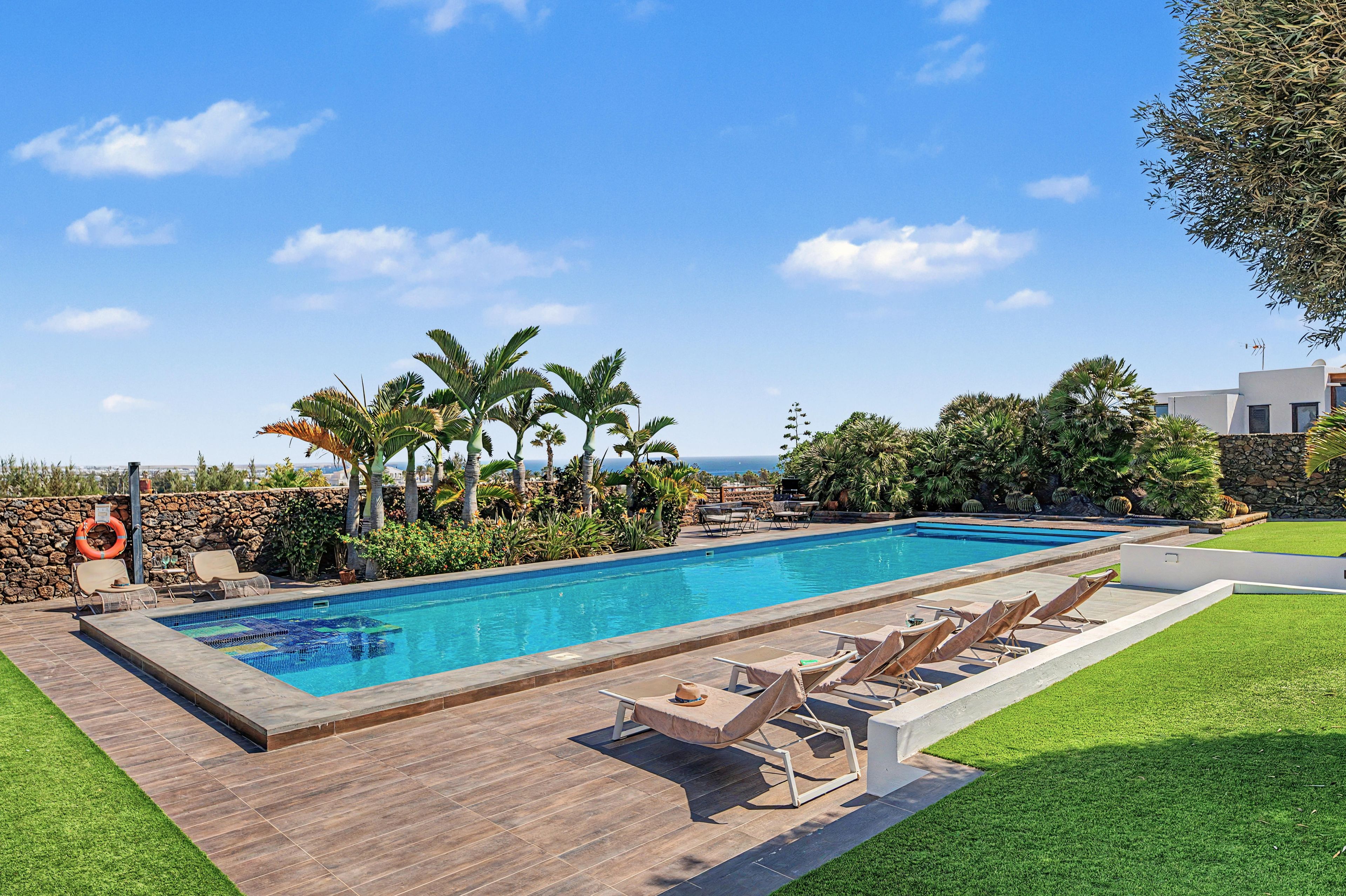 Une piscine rectangulaire bordée de pierres, entourée d’une terrasse en bois et de chaises longues.
