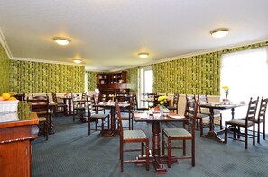 A dining area with multiple tables and chairs, a wooden buffet, and a patterned wallpaper. - Hillgrove Hotel (Dingle)