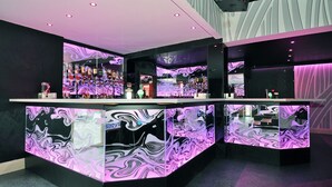 A modern bar area with a central counter and multiple shelves of bottles. - Hillgrove Hotel (Dingle)