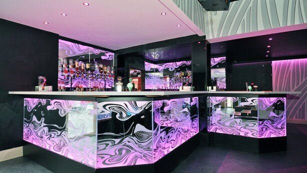 Zona de bar moderna con un mostrador central y varias estanterías llenas de botellas.