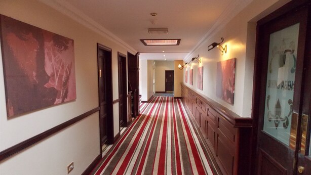 A hotel corridor with a striped carpet, wooden paneling, and artwork on the walls. - Hillgrove Hotel (Dingle)