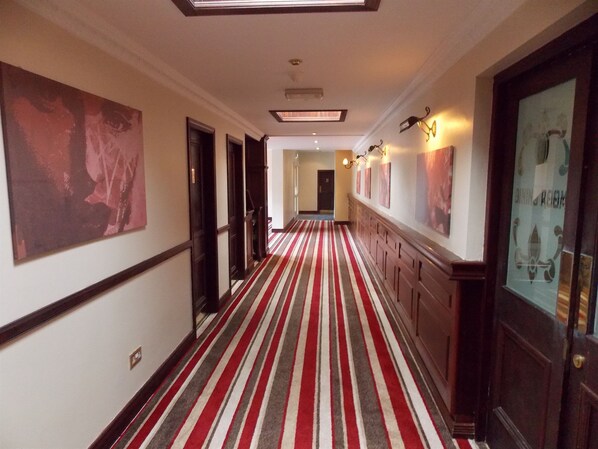 A hotel corridor with a striped carpet, wooden paneling, and artwork on the walls. - Hillgrove Hotel (Dingle)