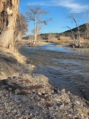 Ein Fluss mit steinigen Ufern und kahl stehenden Bäumen.