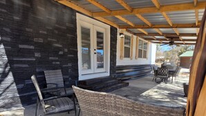 A covered patio with a stone wall, a wicker chair, and a table with a grill. - River Run Retreat on Guadalupe river (Kerrville)