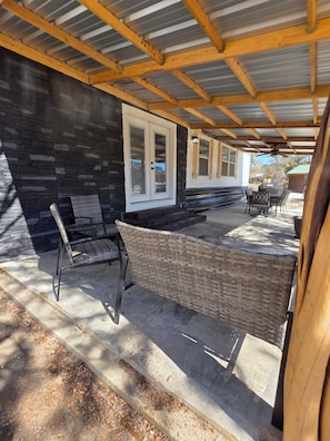Eine überdachte Terrasse mit einer Steinwand, einem Korbstuhl und einem Tisch mit Grill.