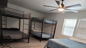 A dormitory room with bunk beds, a ceiling fan, and a window with blinds. - River Run Retreat on Guadalupe river (Kerrville)