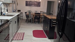 A modern kitchen with a dining area, featuring a central island, pendant lighting, and a large painting on the wall. - River Run Retreat on Guadalupe river (Kerrville)