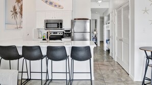 Una cocina moderna con muebles blancos, electrodomésticos de acero inoxidable y una isla central con taburetes de bar.