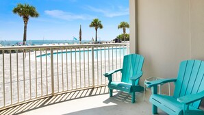Un balcón con sillas Adirondack turquesa, piscina y vista a la playa y al océano.