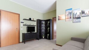Una sala de estar con un sofá, un televisor, un aparador y una estantería de esquina.