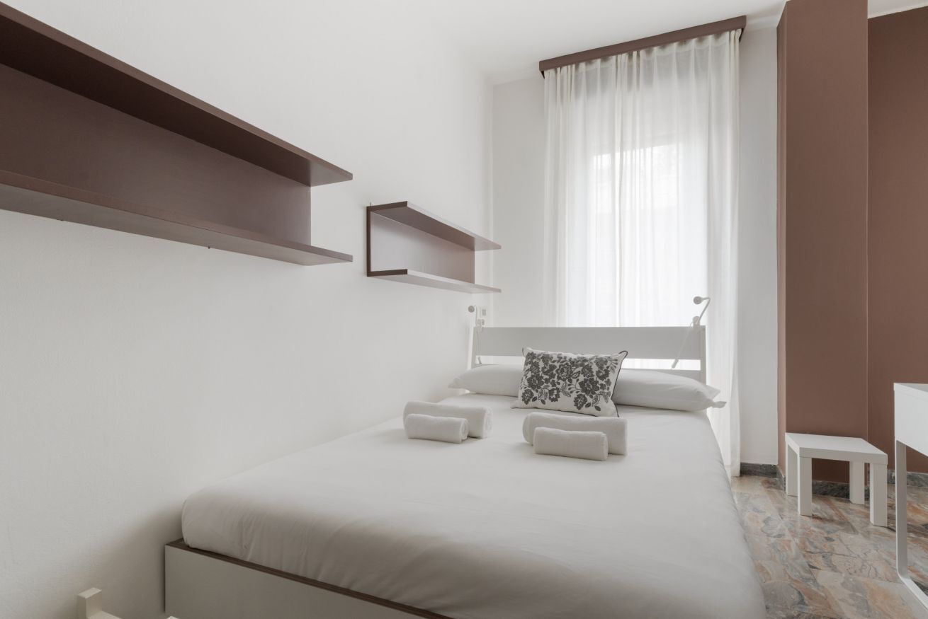 Ein modernes Schlafzimmer mit einem Bett, zwei Nachttischen, einem Fenster mit Vorhängen und eingebauten Regalen.