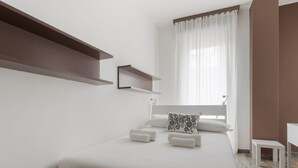Un dormitorio moderno con una cama, dos mesitas de noche, una ventana con cortinas y estanterías empotradas.