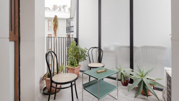Un balcón con dos sillas, una mesita y plantas en macetas.
