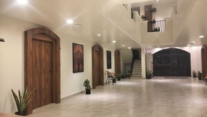 Een ruim interieur met een hoge plafond, houten deuren en een trap naar een hoger gelegen niveau.