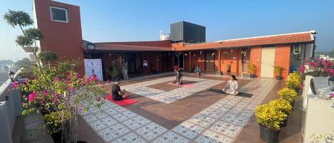 A rooftop with a patterned floor, potted plants, and a building with a red facade.