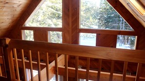 A wooden balcony with a view of trees and a clear sky.
