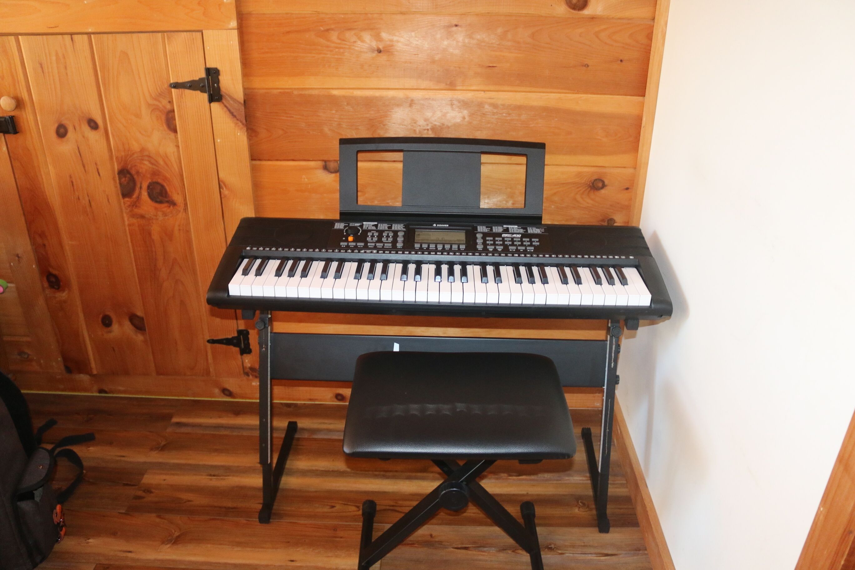A compact keyboard with a bench in a wooden room with a wooden door.