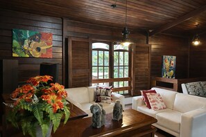Uma sala de estar aconchegante com um sofá branco, uma mesa de centro de madeira e uma janela grande com persianas.