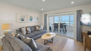 Ein modernes Wohnzimmer mit einem grauen Sofa, einem runden Couchtisch und einem großen Fenster mit Meerblick.