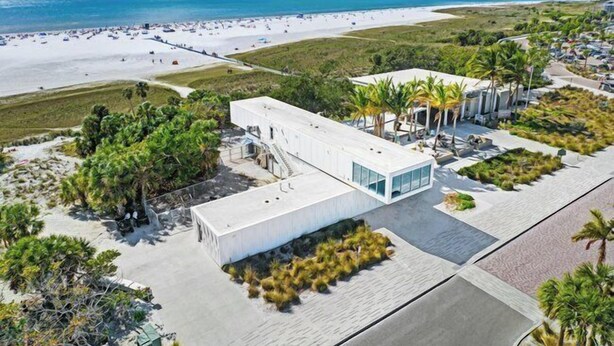 Ein modernes Hotel mit flachem Dach in Strandnähe, mit weißem Sand und klarem, blauem Wasser.