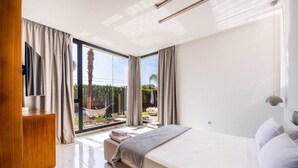 Un dormitorio moderno con una cama grande, un televisor y vistas a un patio exterior con una hamaca y sillones de descanso.