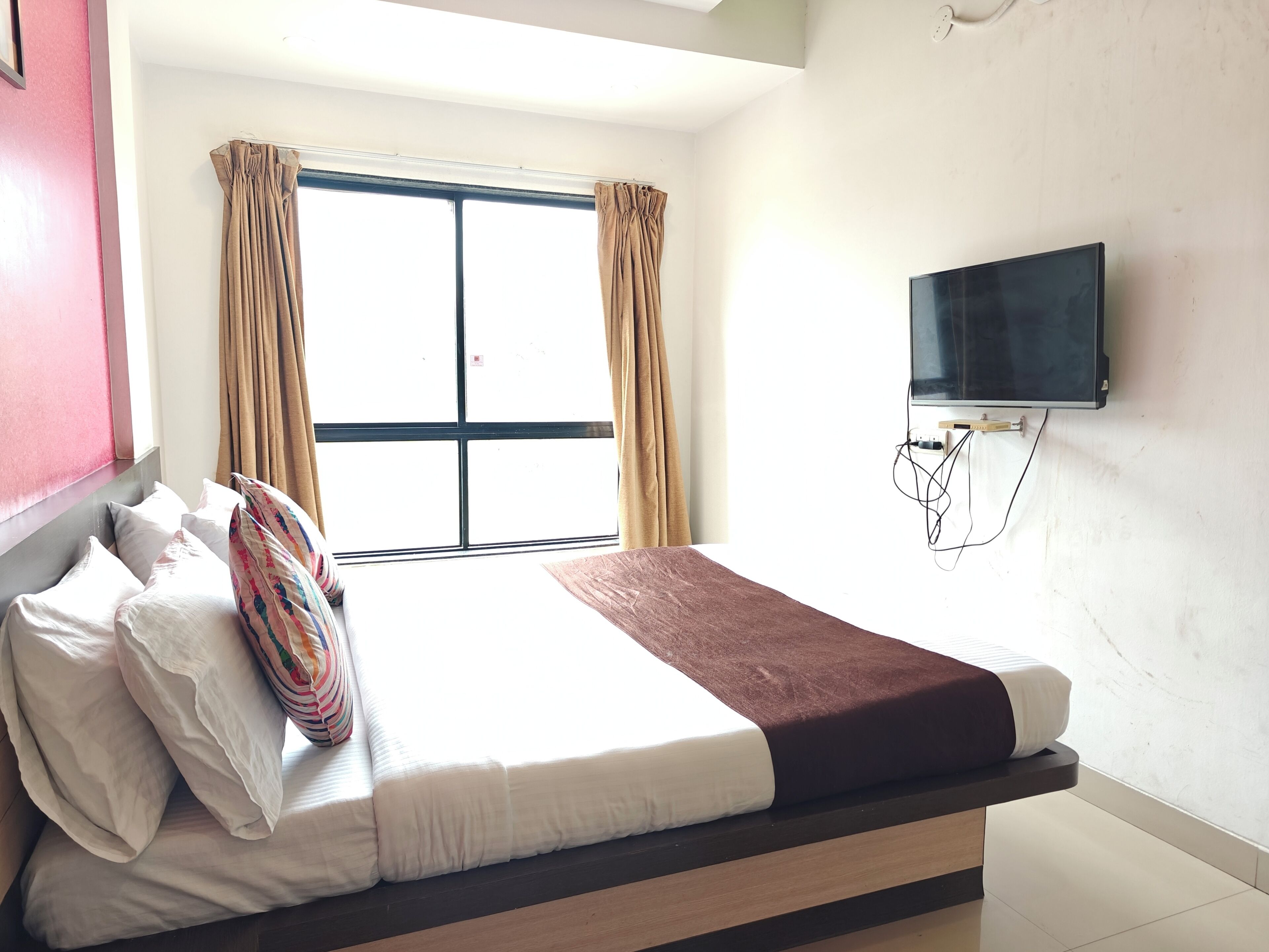 Een hotelkamer met een bed, een aan de muur bevestigde televisie en een raam met gordijnen.