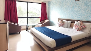 Una habitación de hotel con una cama grande, un escritorio, una silla y un ventanal con cortinas.