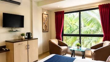 Ein Hotelzimmer mit Bett, Fernseher, Schreibtisch, Stuhl, Tisch und einem Fenster mit Vorhängen.