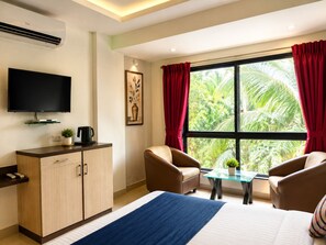 A hotel room with a bed, a TV, a desk, a chair, a table, and a window with curtains. - Hotel Amruta Executive (Bhor)