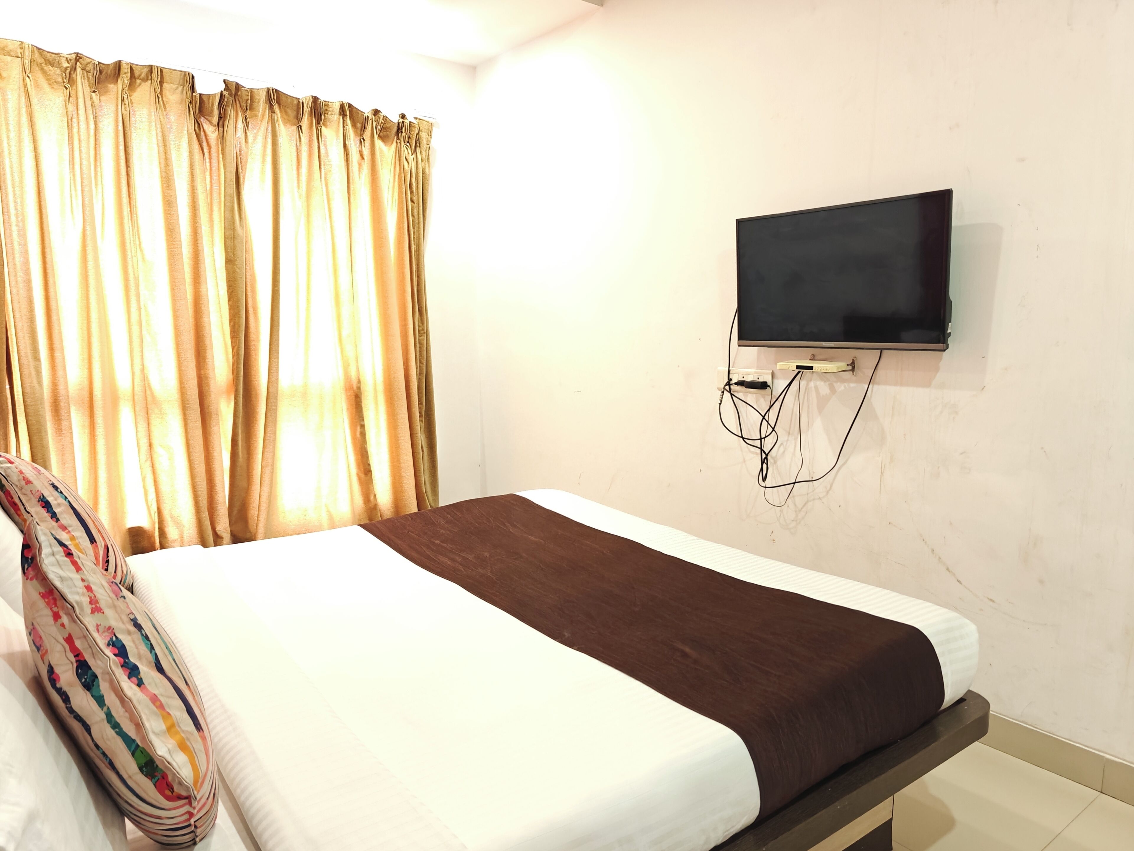 A hotel room with a bed, a TV mounted on the wall, and a window with curtains.