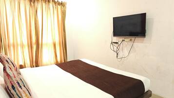 A hotel room with a bed, a TV mounted on the wall, and a window with curtains.