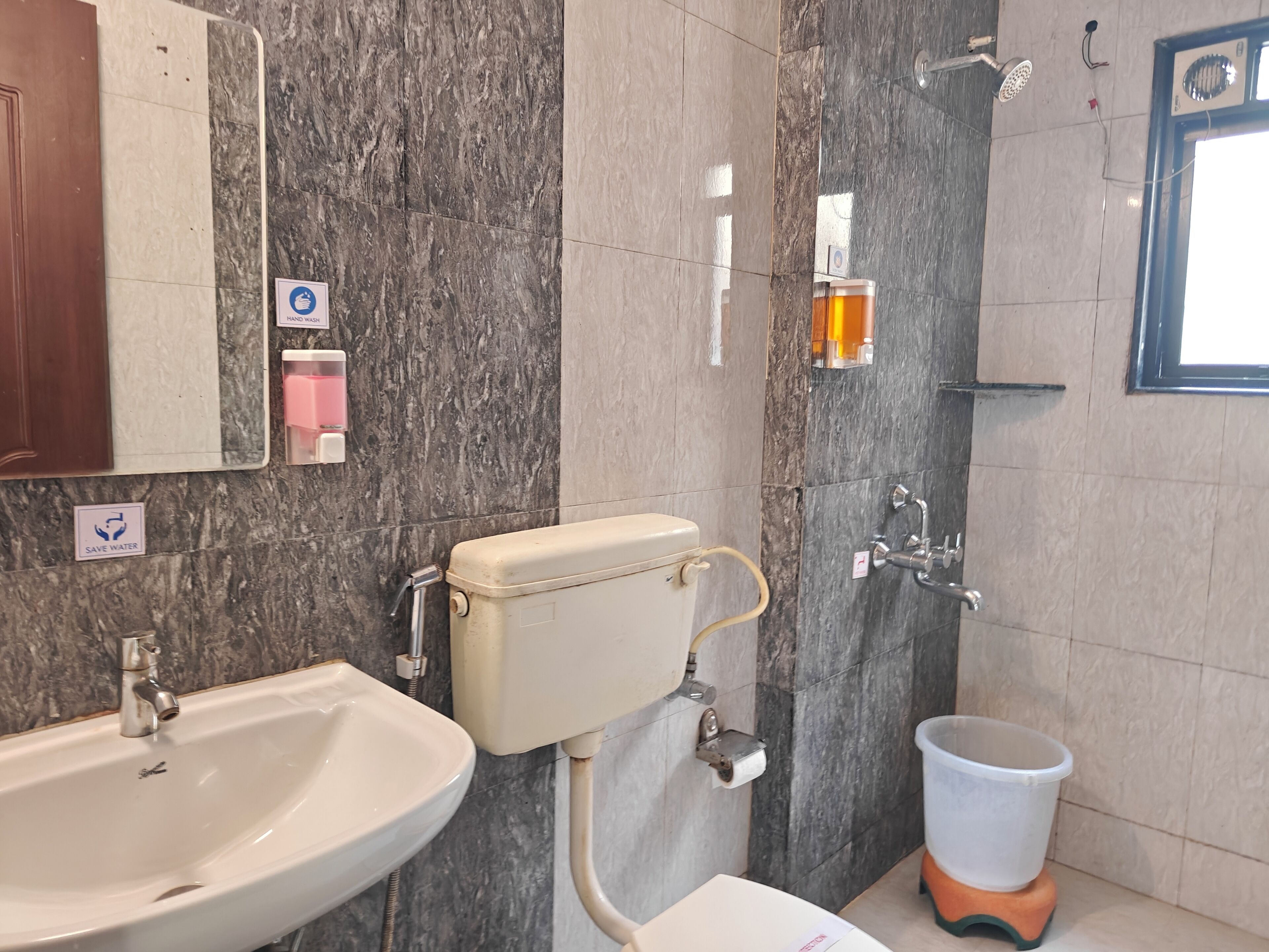 A bathroom with a sink, toilet, and shower. There are hand wash facilities and a 'Save Water' sign.
