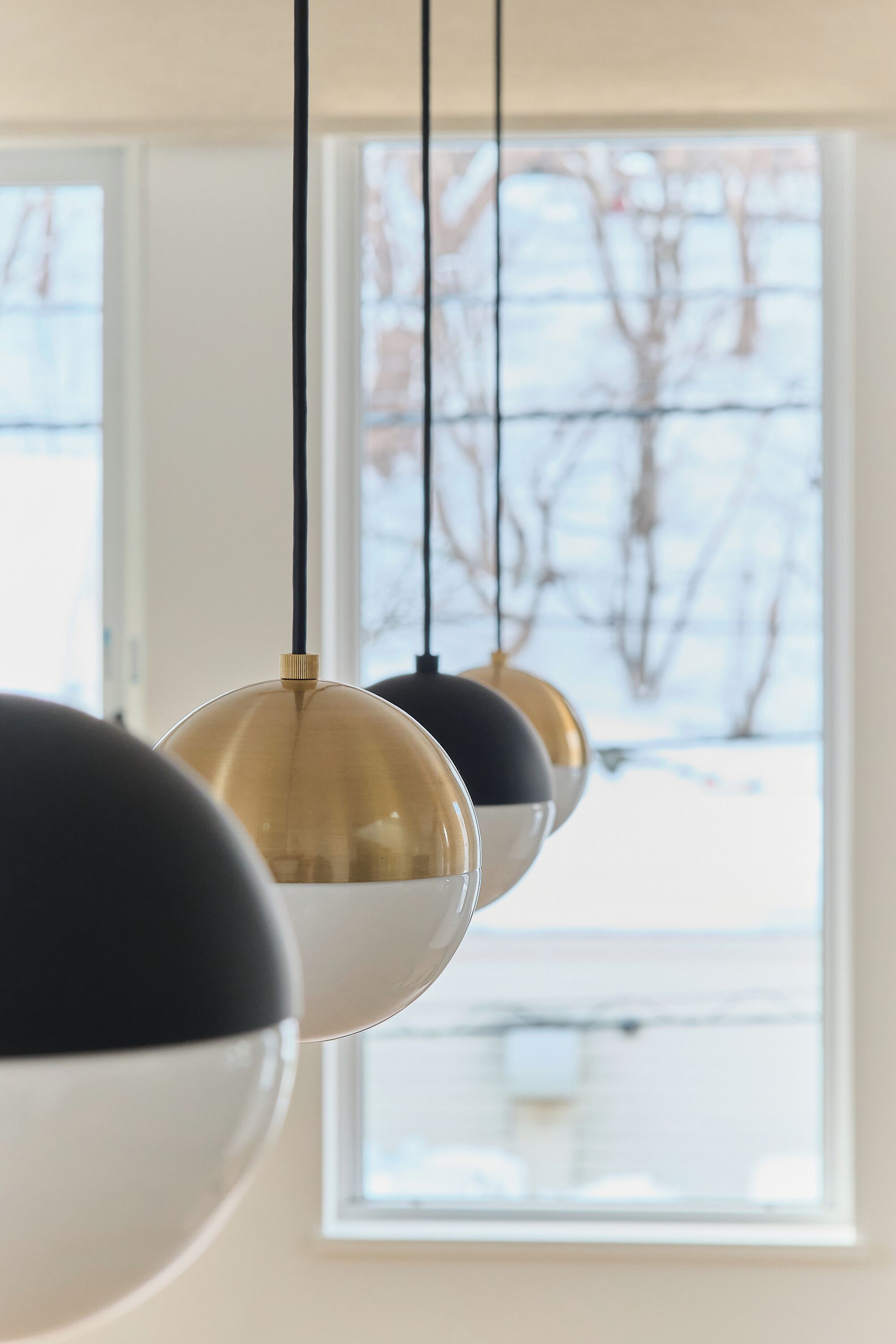 A row of spherical pendant lights with black and gold finishes, hanging from a ceiling in a room with large windows.