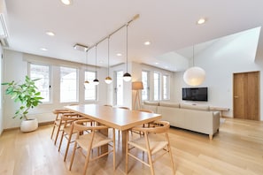 A spacious dining area with a long wooden table and chairs, a potted plant, and a modern pendant light.