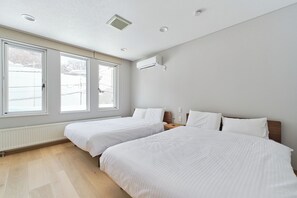A bedroom with two beds, large windows, a radiator, and a wall-mounted air conditioner.
