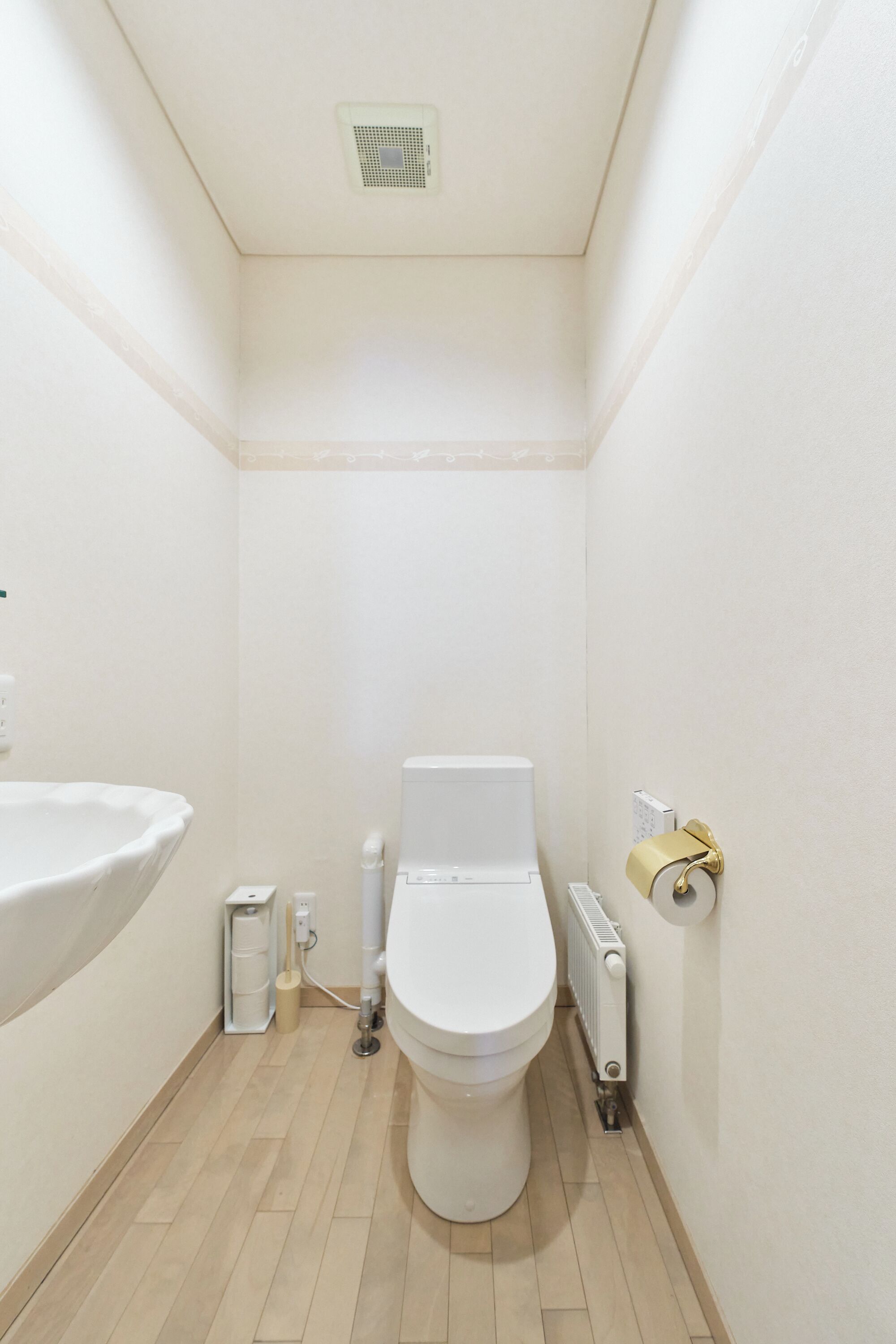 A small, narrow bathroom with a white toilet, a white sink, and a radiator.