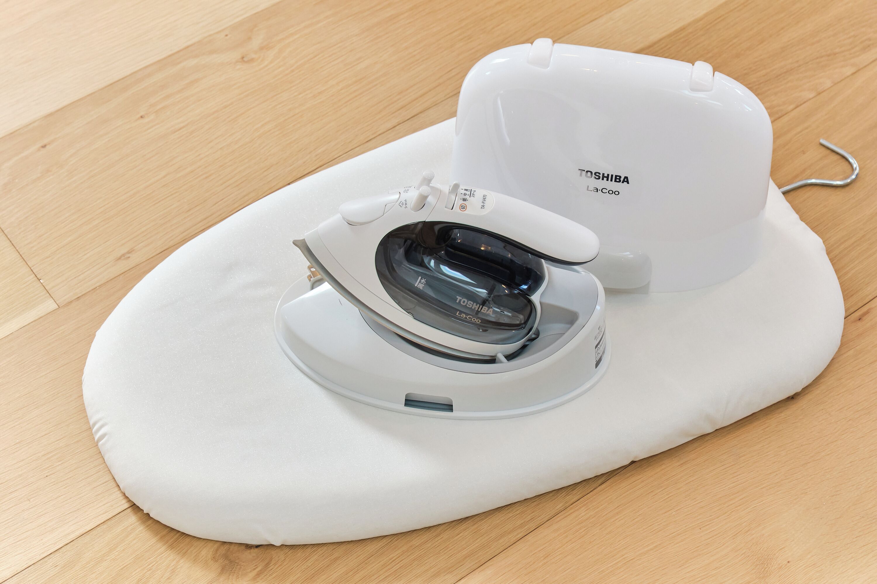 A white portable iron with a control panel and a power cord on a wooden floor.