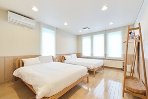 Habitación de hotel con dos camas individuales, suelo de madera, aire acondicionado de pared y ventana con vistas.