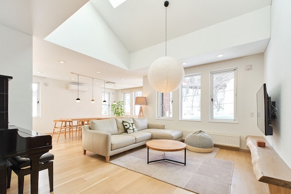 A spacious living room with a piano, a sofa, a coffee table, and a dining area in the background.
