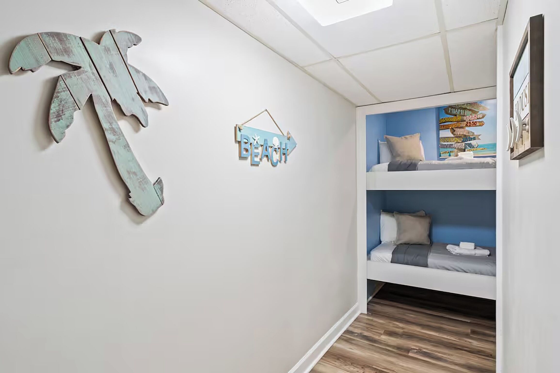 A room with a bunk bed, a wall-mounted sign reading "BEACH," and a decorative wooden palm tree.