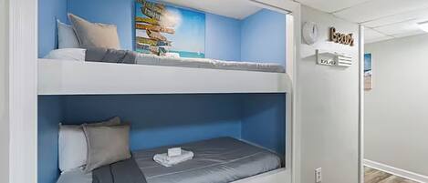 Ein Schlafraum mit Etagenbetten, blauer Wand und einem Poster einer tropischen Landschaft.