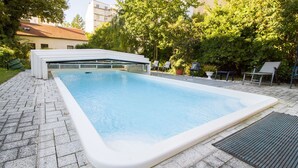 Une piscine extérieure rectangulaire, bordée de blanc, entourée d’une zone pavée et agrémentée d’une grille métallique.