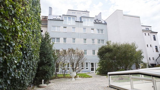 Ein mehrstöckiges Gebäude mit Innenhof, umgeben von Grünflächen und einem gepflasterten Weg.