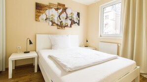 Ein Schlafzimmer mit einem großen Bett, zwei Nachttischen, einem Wandbild von weißen Orchideen, einem Fenster mit Vorhängen und einem Heizkörper.