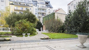 Une cour avec un chemin pavé, une statue et diverses plantes.