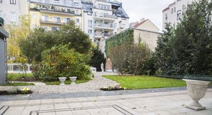 Une cour avec un chemin pavé, une statue et diverses plantes.
