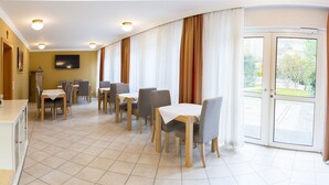 Ein Essbereich mit Tischen und Stühlen, ein Fernseher an der Wand und Blick durch Glastüren.