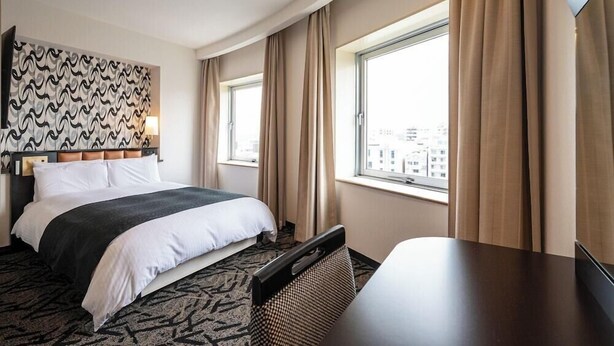 A hotel room with a large bed, a desk, and a view of the city through the window. - APA Hotel Shonan Tsujido Ekimae (Fujisawa)