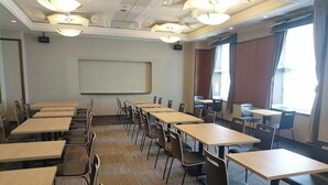 A conference room with multiple tables and chairs, a projector screen, and large windows with curtains. - APA Hotel Shonan Tsujido Ekimae (Fujisawa)